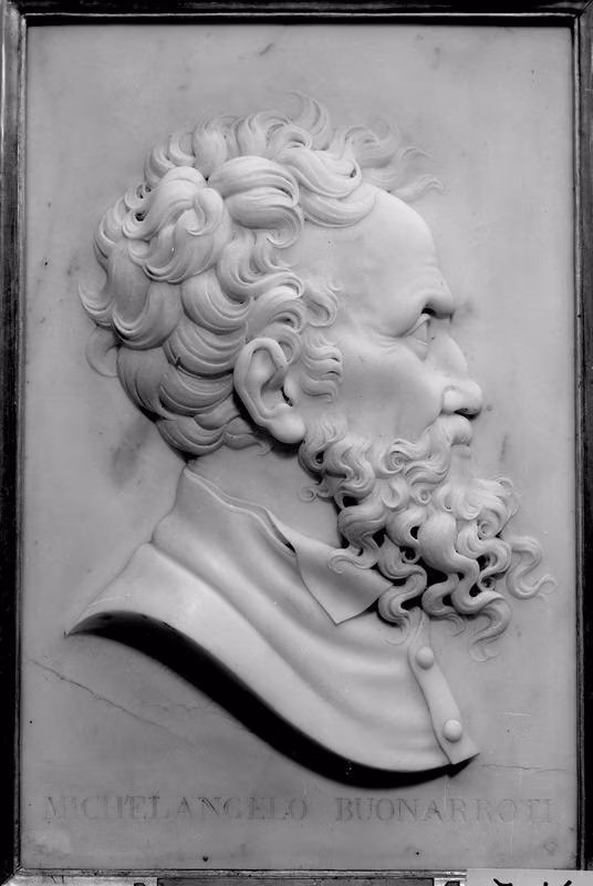 Un rilievo in marmo mostra il profilo dettagliato di un uomo con barba e capelli ricci, il tutto inserito in una cornice rettangolare.