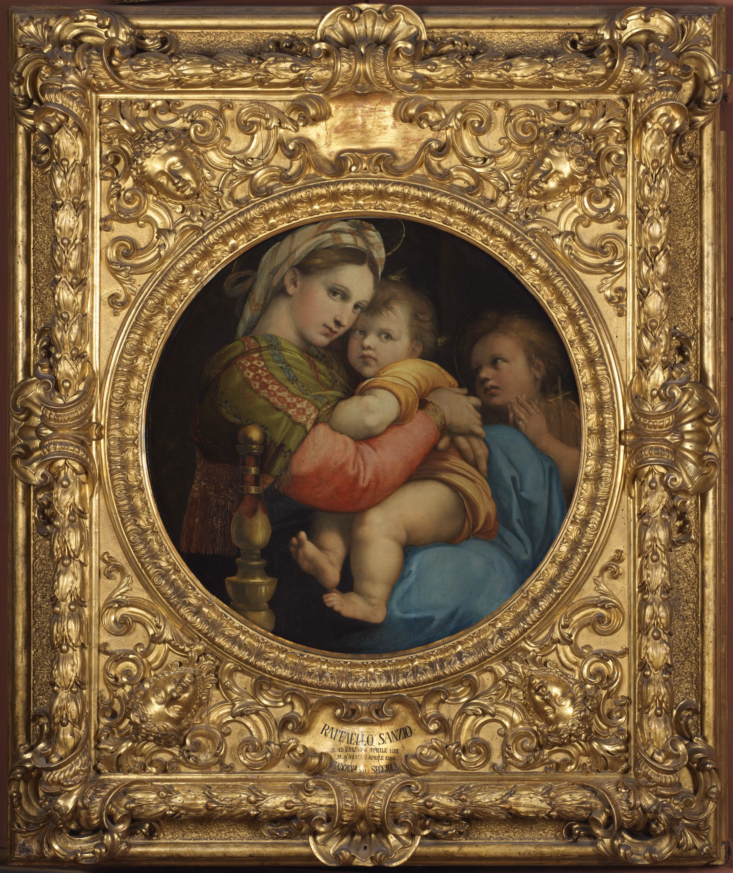 A detailed, ornate gilded frame encases a classical painting depicting a serene scene of a woman holding a child, with intricate gold designs and embellishments enhancing the artwork's elegance and historical significance.