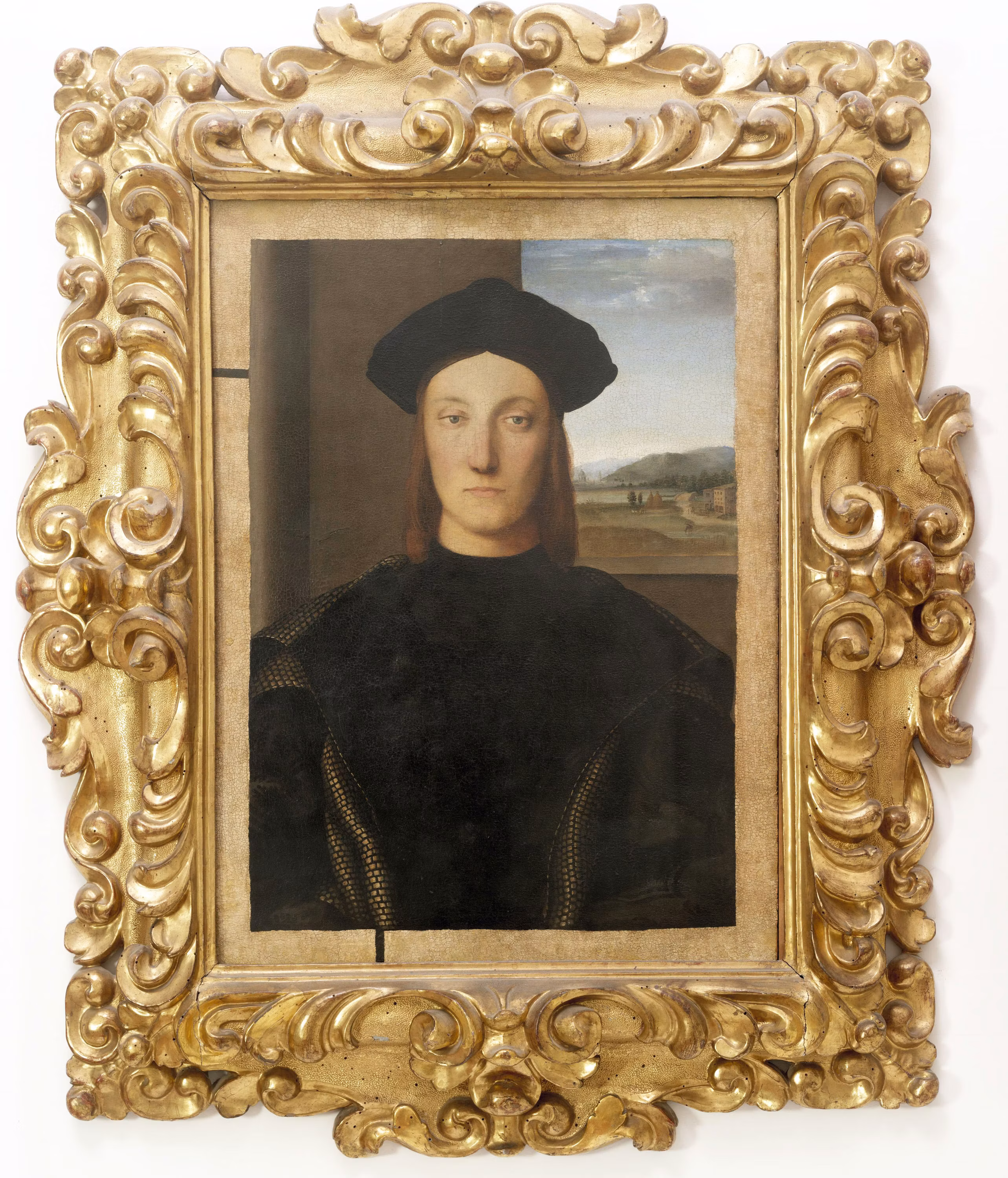 Un dipinto rinascimentale raffigurante un giovane vestito di nero, incorniciato da una cornice dorata riccamente decorata, esposto in un museo con un paesaggio visibile sullo sfondo.