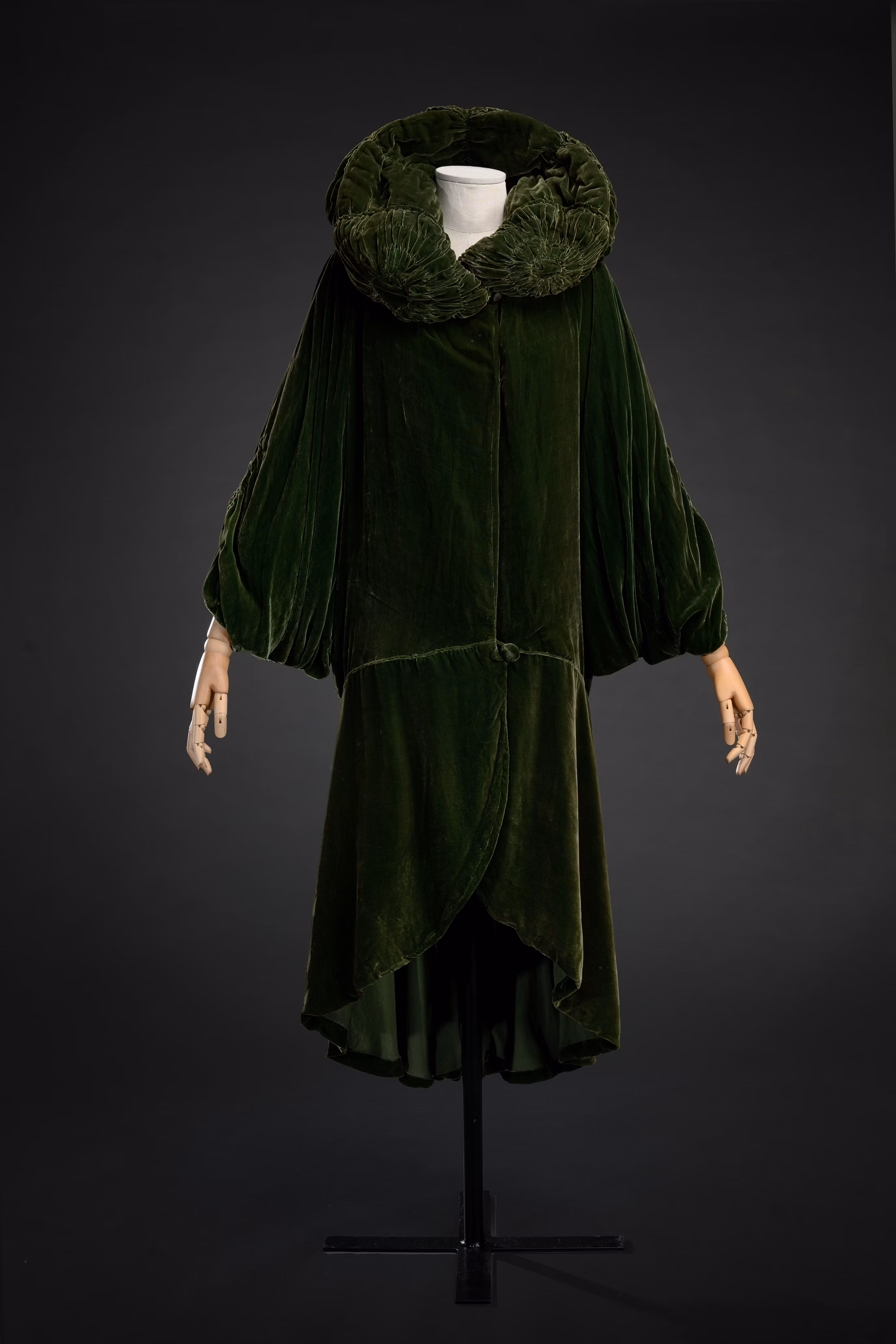 Abito in velluto verde scuro con collo ampio e maniche a sbuffo, ambientato su sfondo nero.
