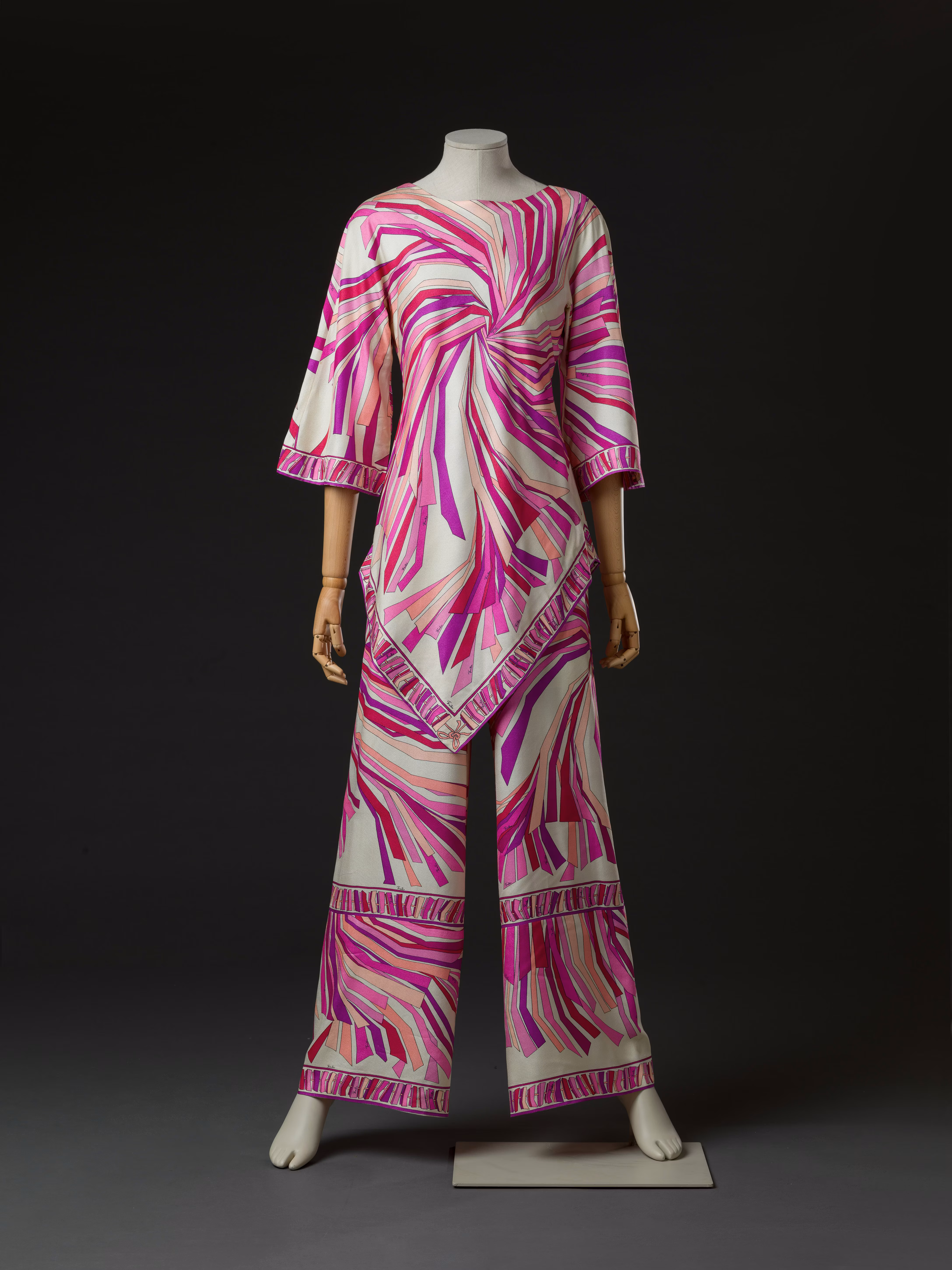 A mannequin showcases a vibrant women's ensemble featuring a pink and white abstract swirl pattern, consisting of a knee-length tunic with elbow-length sleeves and matching wide-leg pants, set against a dark background.