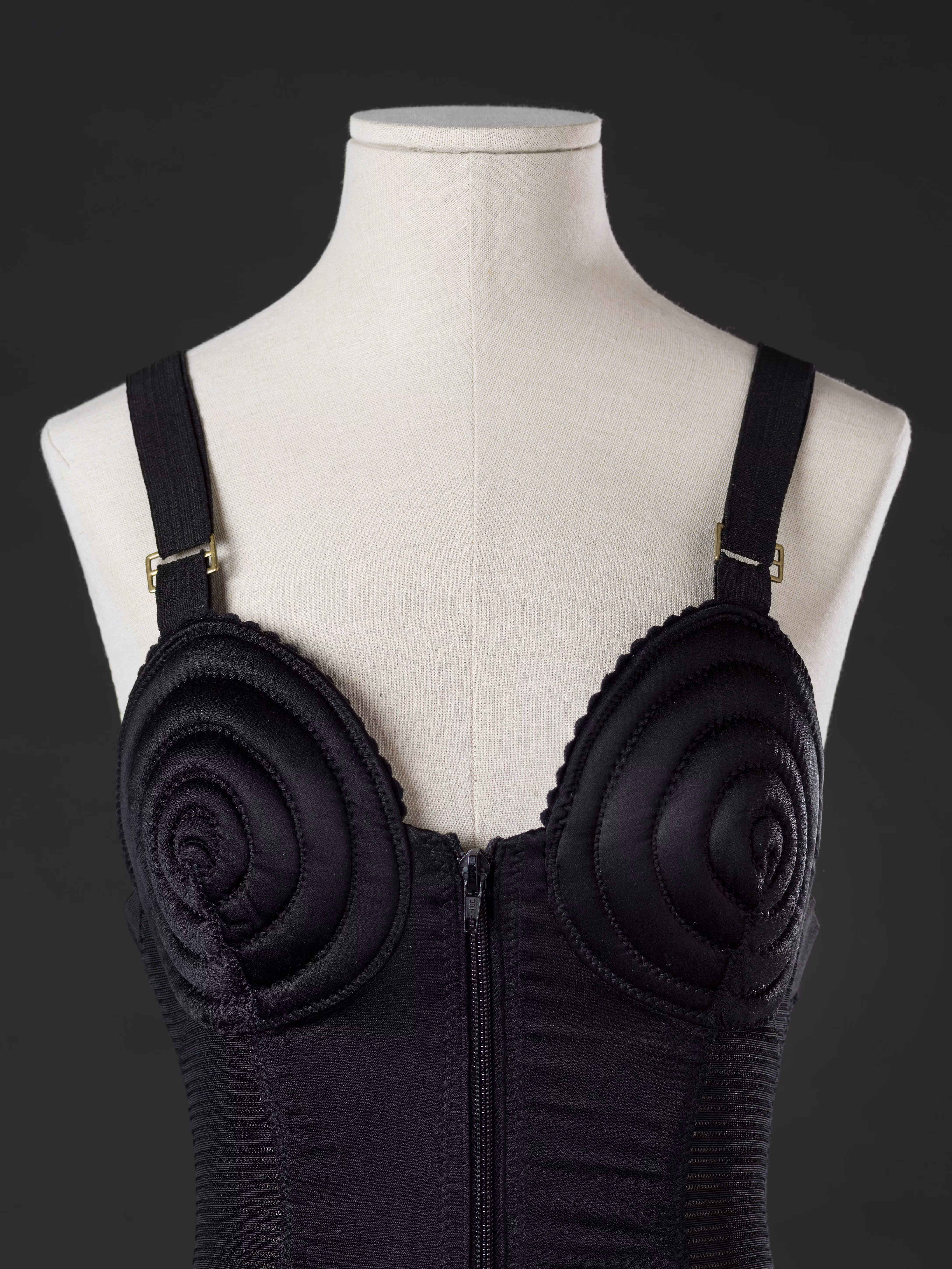 A black corset with spiral stitching details on the bust is displayed on a mannequin against a dark background.