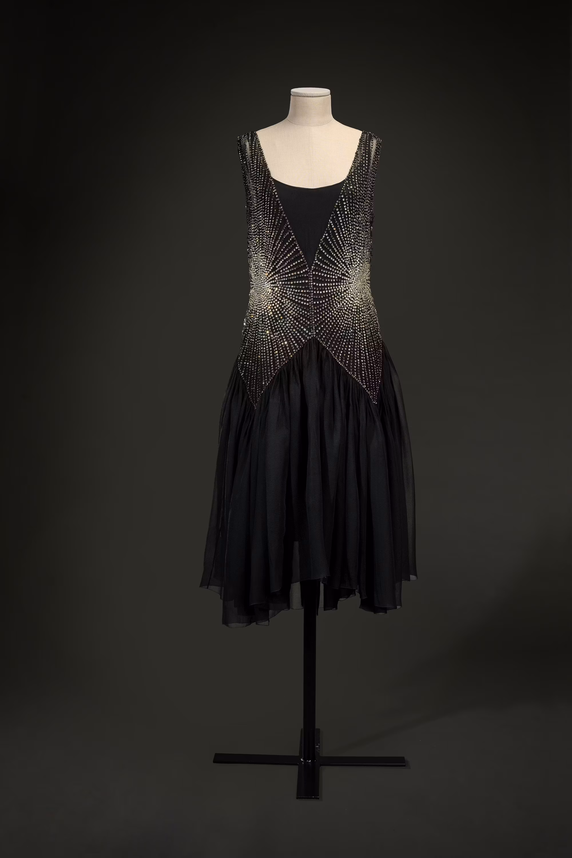 Un elegante abito nero con dettagli intricati e scintillanti in paillettes e perline, esposto su un manichino su sfondo scuro.